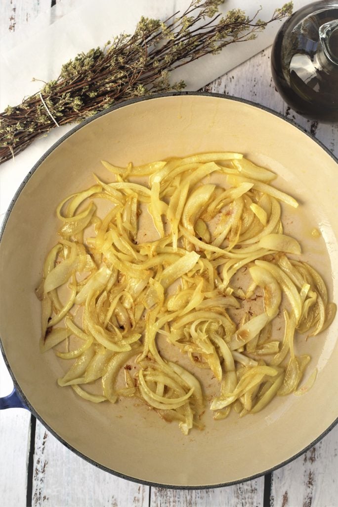 large skillet with sautéd sliced onion with oregano branches and olive oil on side 