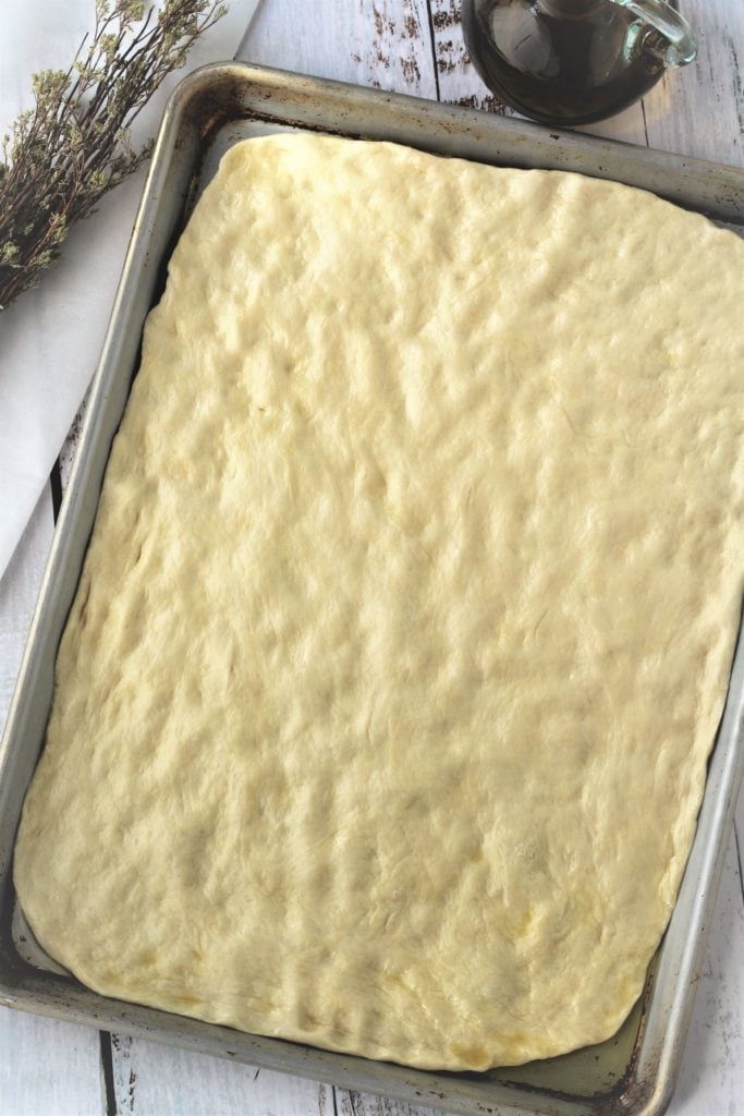 flattened pizza dough in rectangular baking sheet 