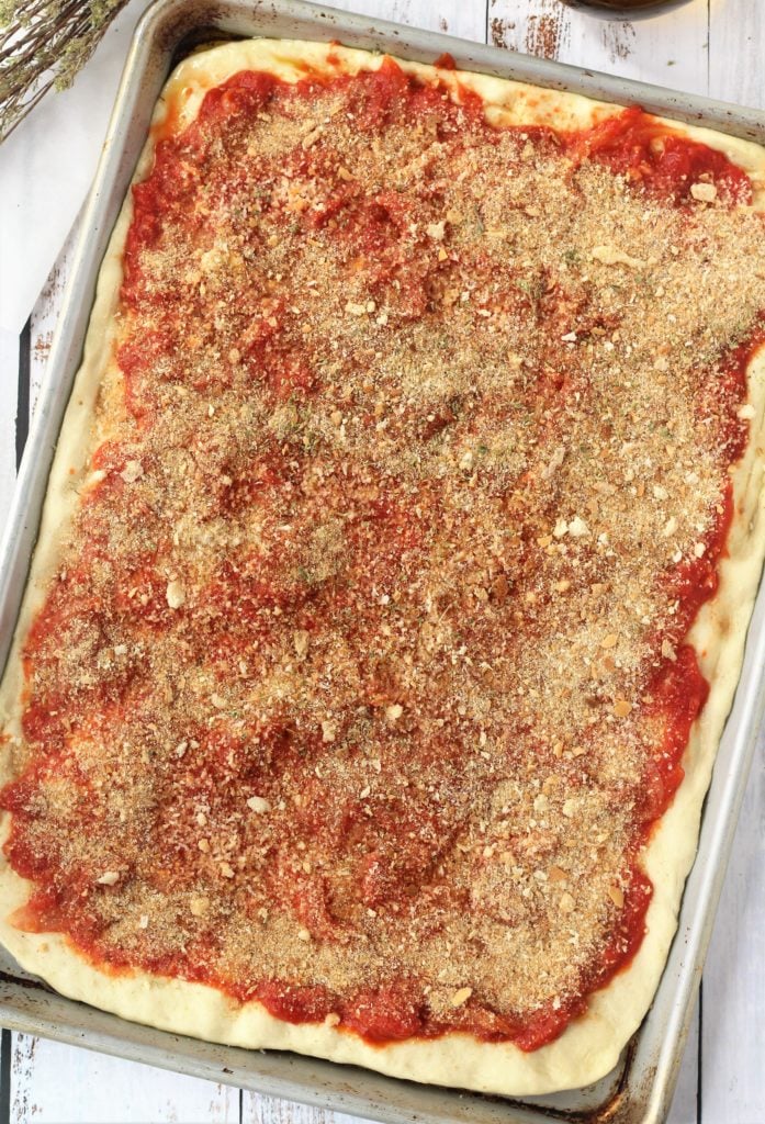 rectangular pizza dough topped with tomato sauce and breadcrumbs 