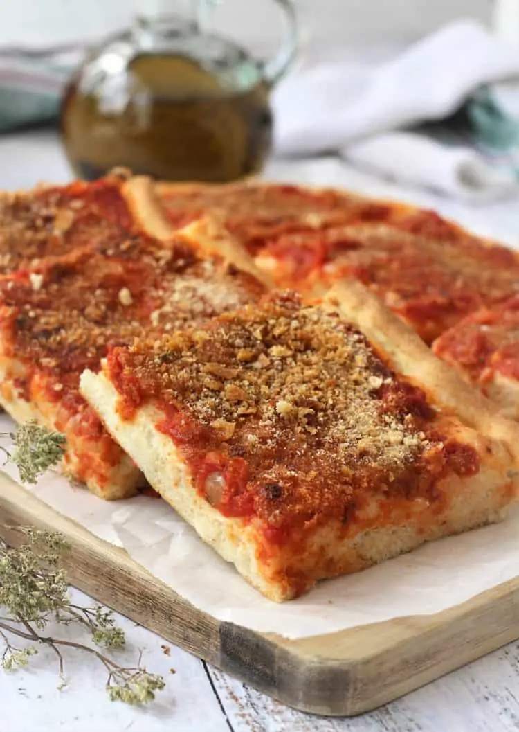 tomato and breadcrumb topped pizza squares overlapped on wood board with oregano branches on side
