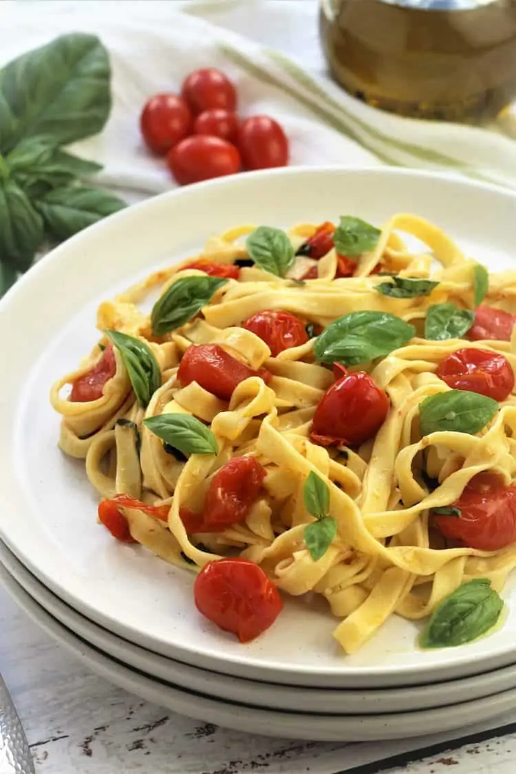white plate filled with tagliatelle pasta with cherry tomatoes and basil leaves
