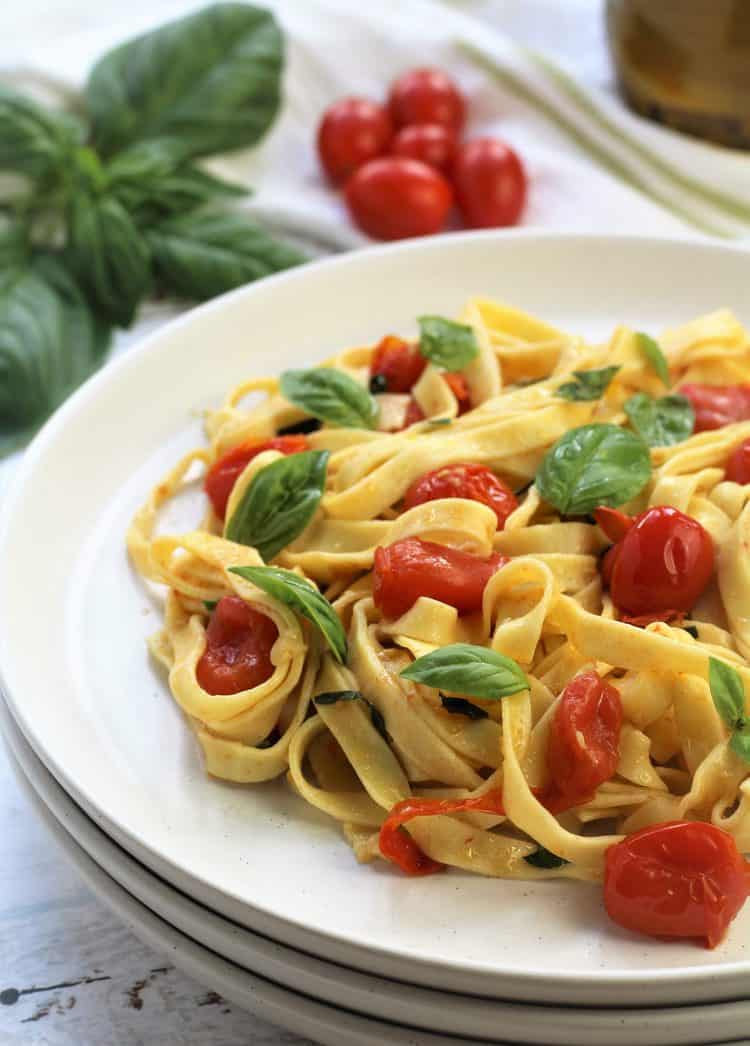 white plate filled with tagliatelle with cherry tomatoes and fresh basil