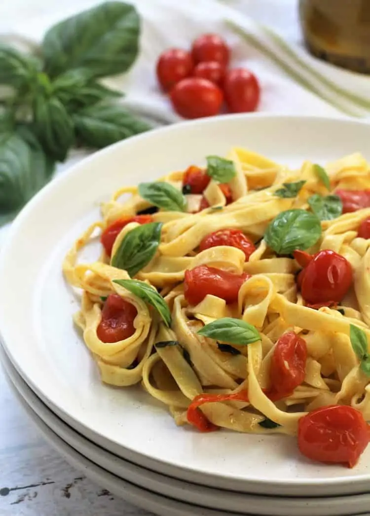white plate filled with tagliatelle with cherry tomatoes and fresh basil