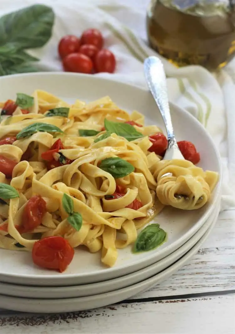 fork twirled with tagliatelle pasta on plate with tagliatelle, cherry tomatoes and basil leaves