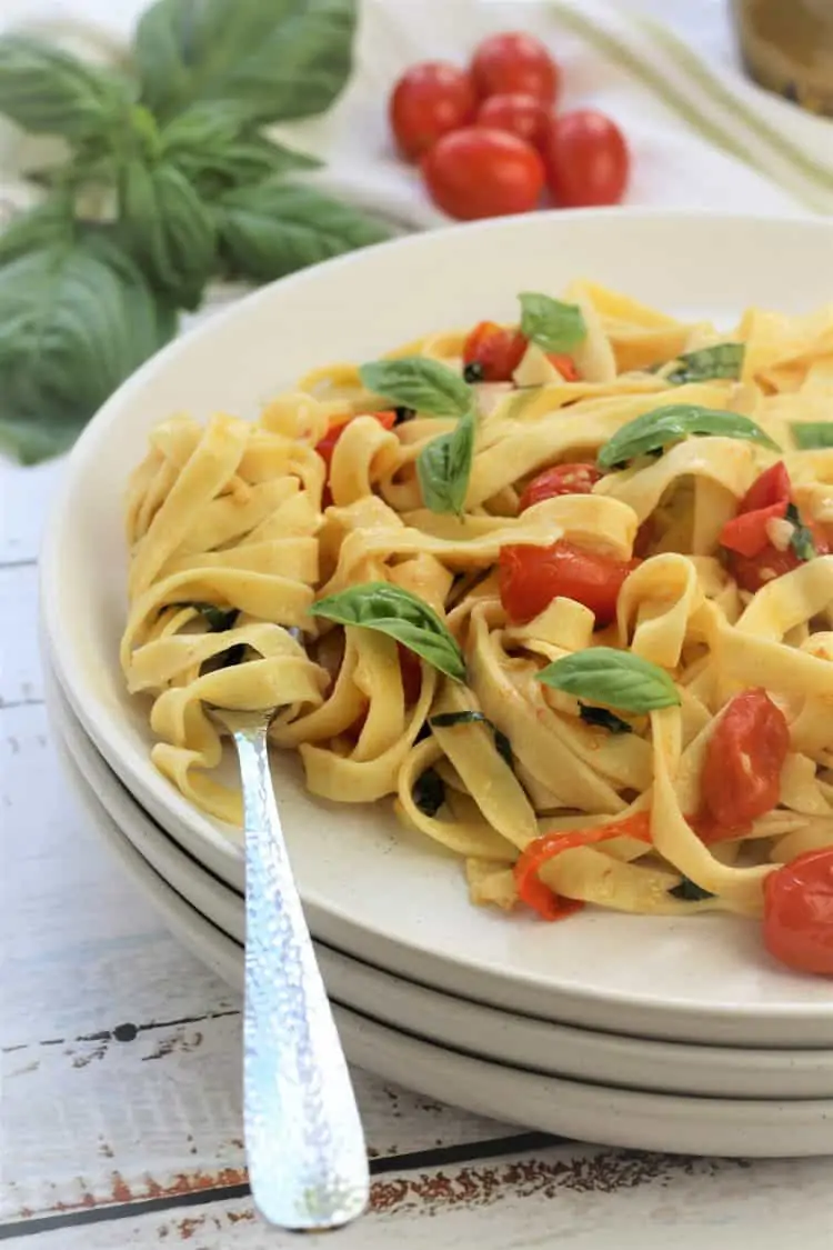 forkful with twirled tagliatelle on white plate with pasta, cherry tomatoes and fresh basil