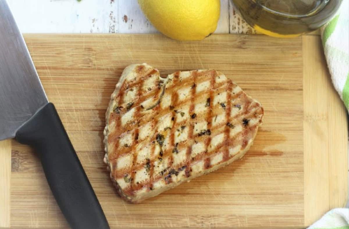 Grilled tuna steak on cutting board with knife, lemon and olive oil bottle.