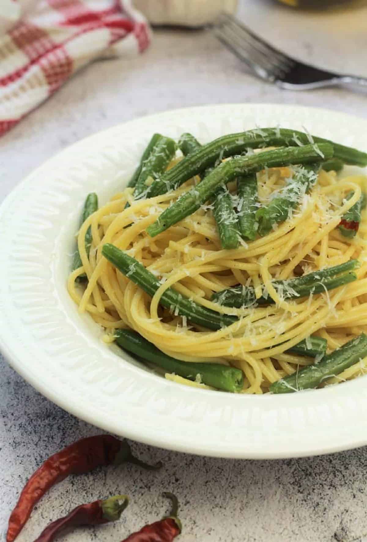 Spaghetti with green beans topped with grated cheese in white bowl.