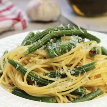 Spaghetti with green beans plated and topped with grated cheese.