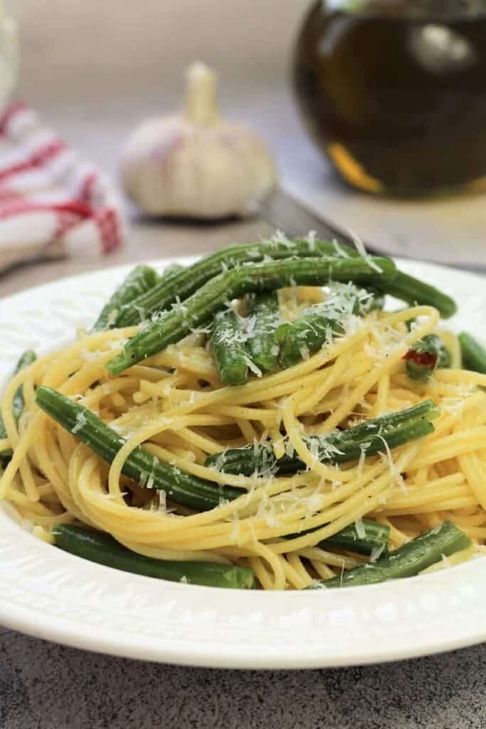 Spaghetti with green beans plated and topped with grated cheese.