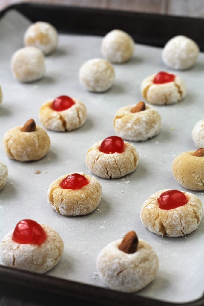 baking sheet filled with unbaked almond and cherry topped amaretti cookies