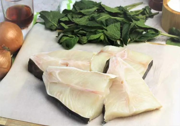 fresh halibut steaks on parchment paper surrounded by mint leaves, onions and glass with vinegar