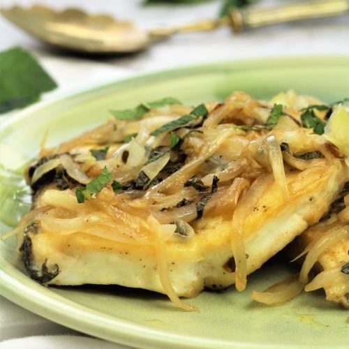 halibut steak topped with onions and mint on green plate