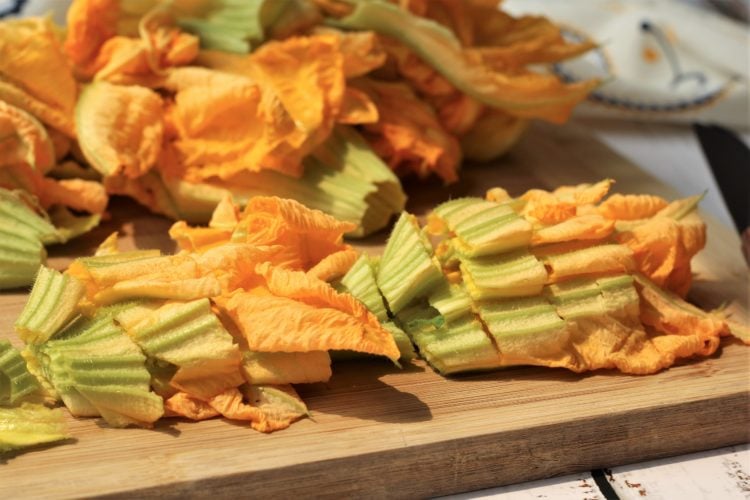 Chopped zucchini blossoms on wood board.