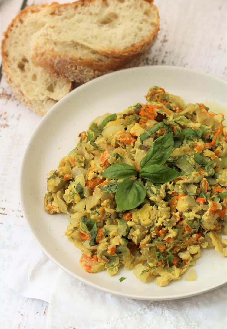 white plate with scrambled eggs with zucchini blossoms and sliced bread