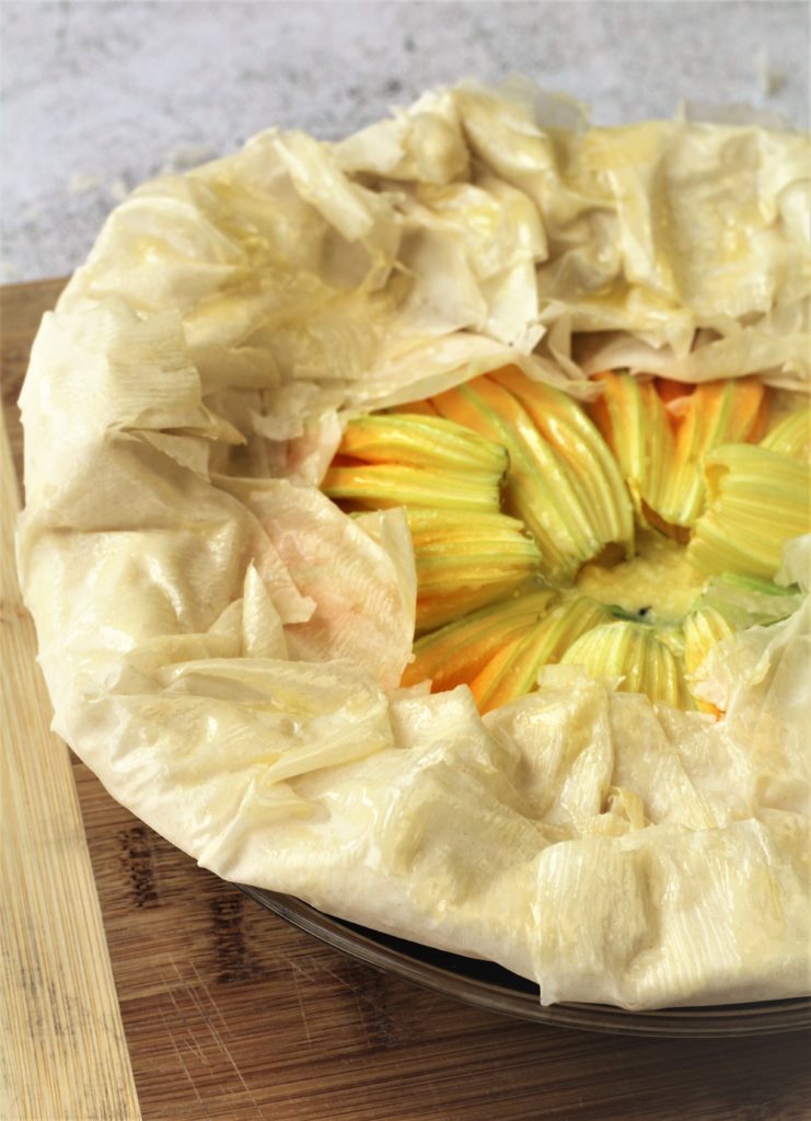 filo dough folded over zucchini blossoms in pie plate