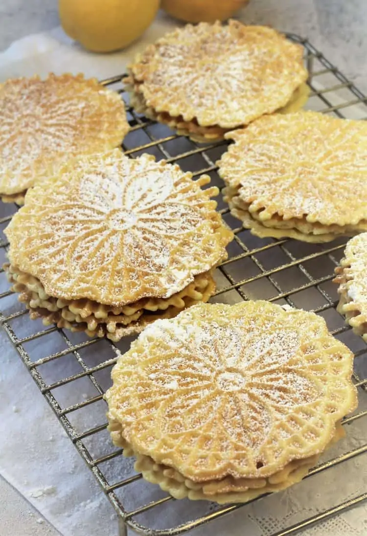 stacked pizzelle dusted with powdered sugar on wire rack