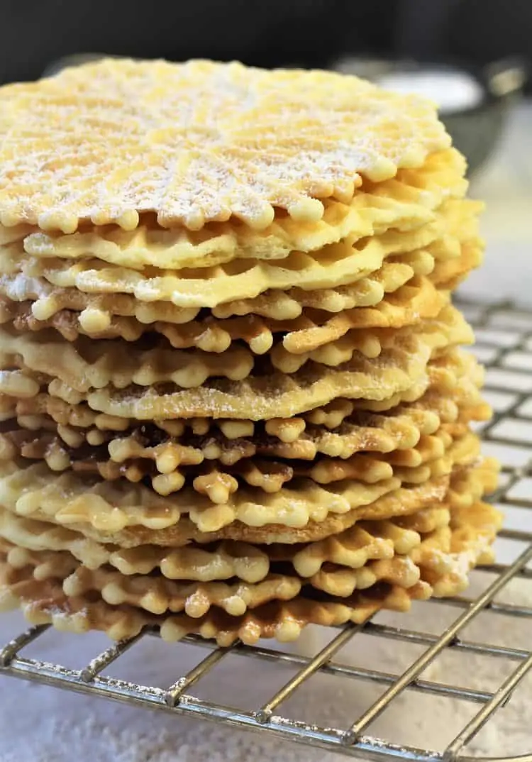 stacked italian pizzelle cookies dusted with powdered sugar on wire rack