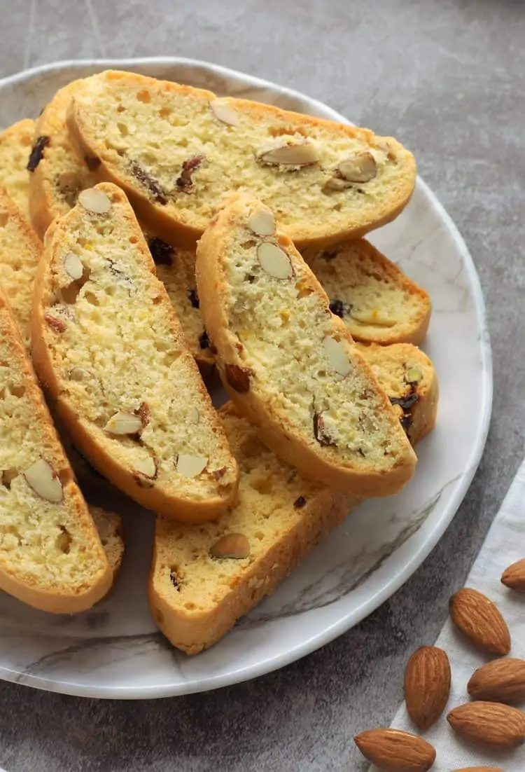 almond biscotti piled onto a white plate with almonds around it