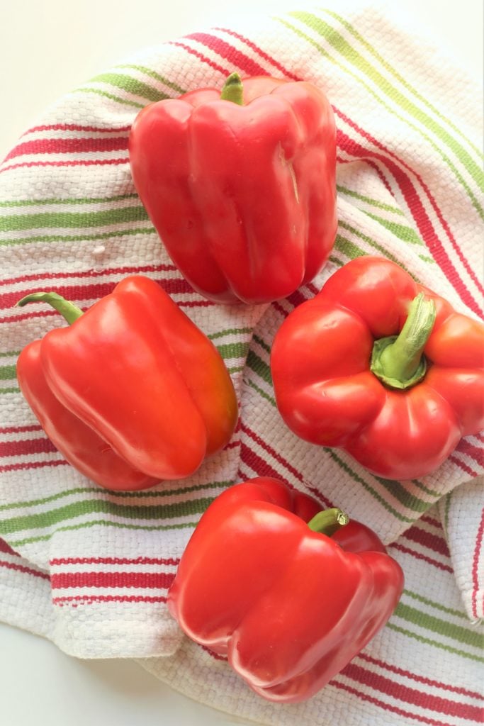 4 red bell peppers on striped kitchen towel