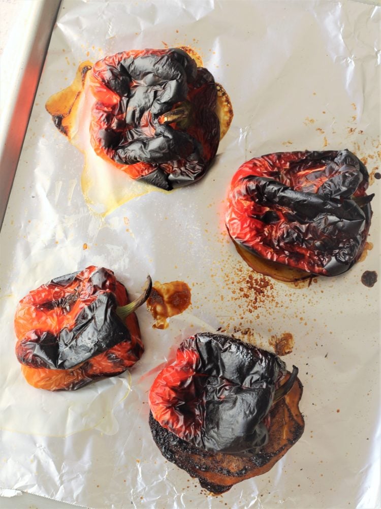 4 charred red bell peppers on foil lined baking sheet