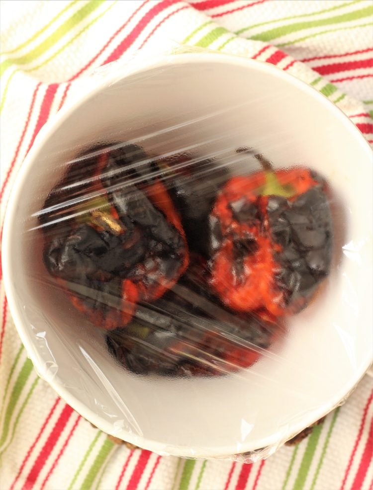charred red bell peppers in bowl covered with wrap