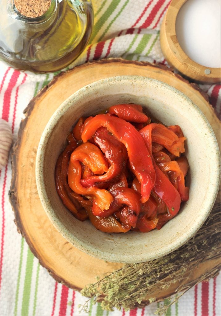 roasted red bell pepper strips in bowl surrounded by olive oil, salt, garlic and oregano