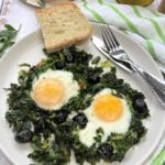 fried eggs with sautéed greens on plate with slice of bread and utensils