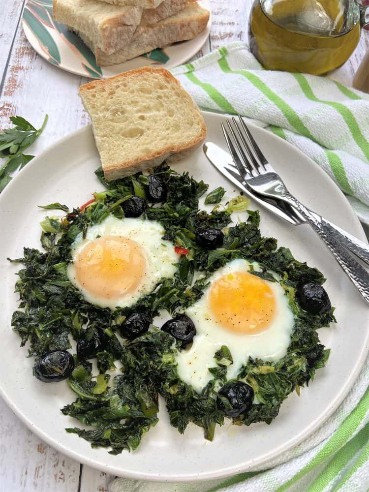 plate with 2 fried eggs and greens with slice of bread and utensils