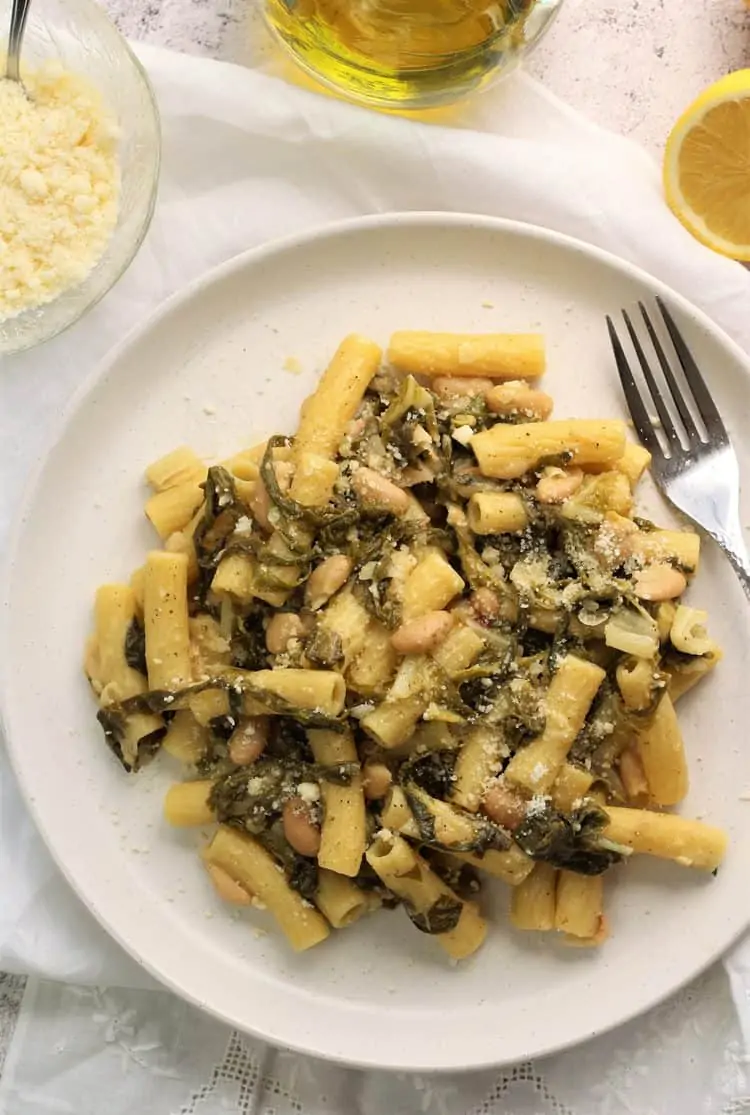 white plate filled with pasta, swiss chard and beans with fork on side