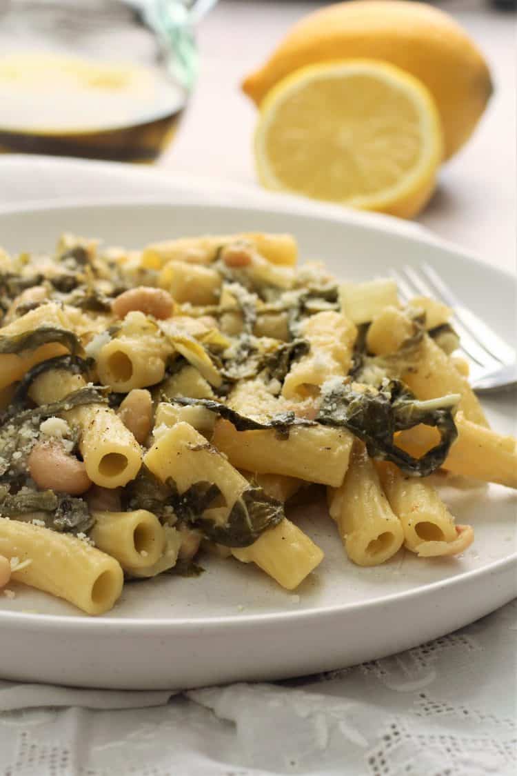 pasta with swiss chard and white beans topped with cheese in white plate 