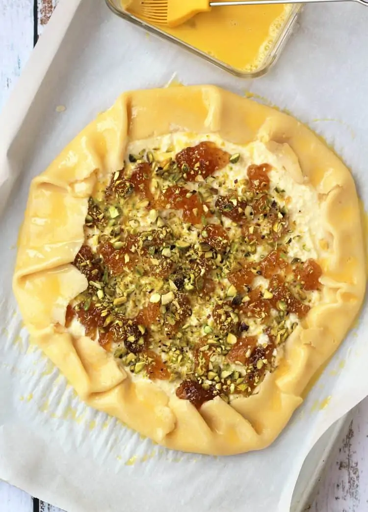 crostata topped with ricotta, fig jam and pistachios on parchment paper