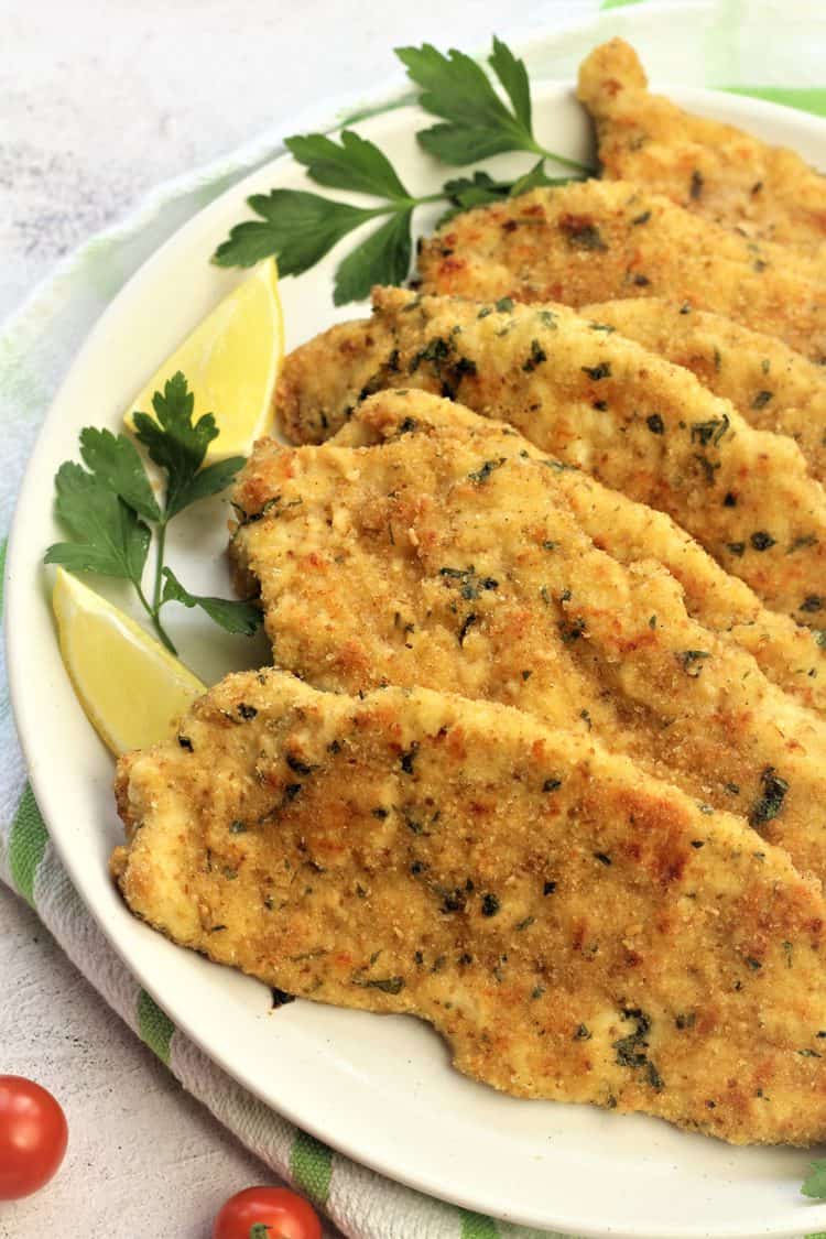 overhead view of white plate with chicken cutlets, parsley and lemon wedges