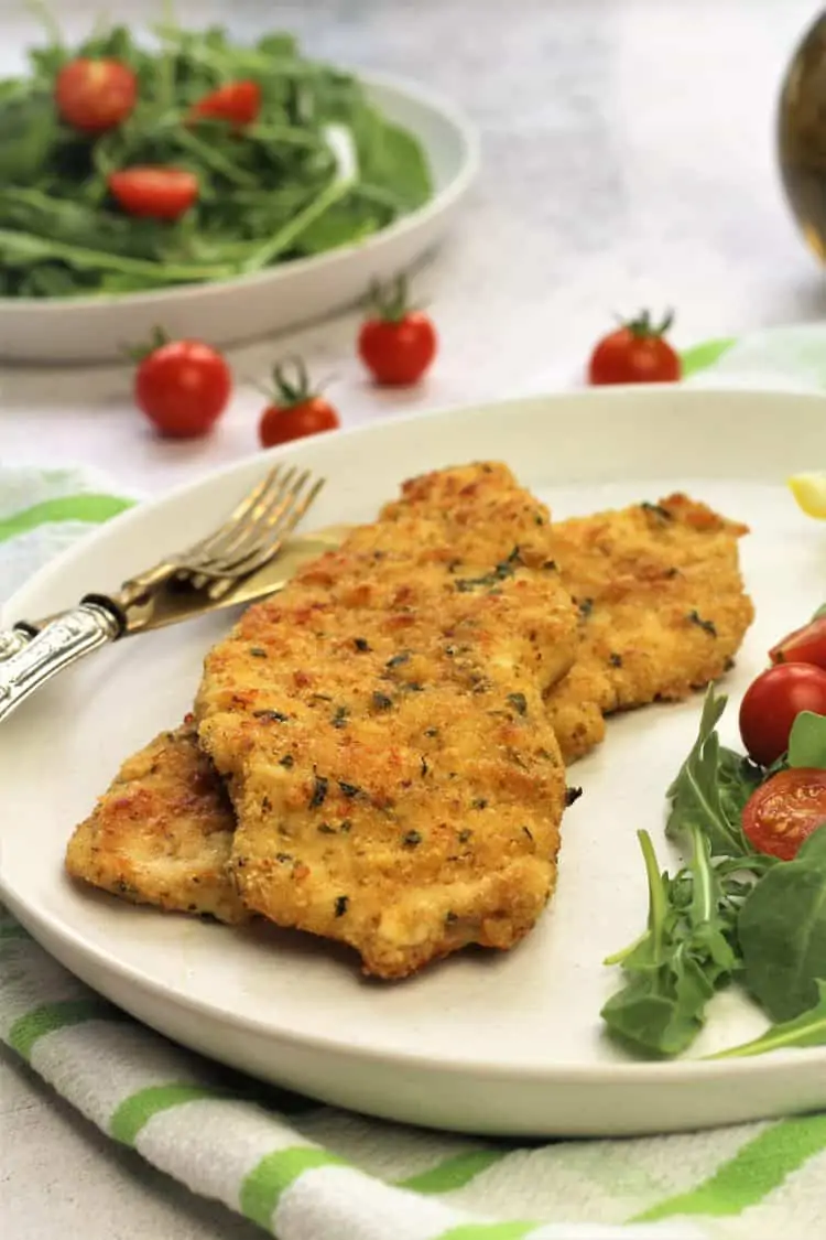 chicken cutlets on plate with arugula and tomato salad