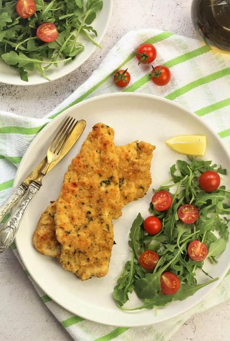 chicken cutlets with arugula and tomato salad on white plate with cutlery