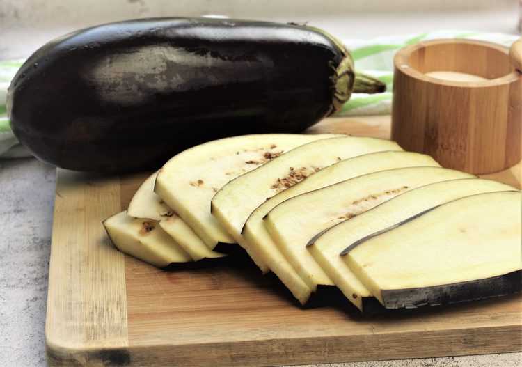 thinly sliced eggplant on wood board with large whole eggplant