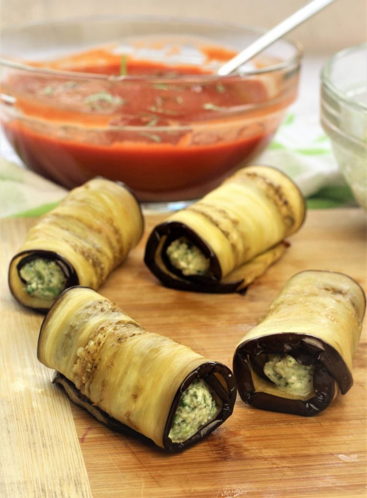 eggplant involtini filled rolls on wood board with bowl of sauce 