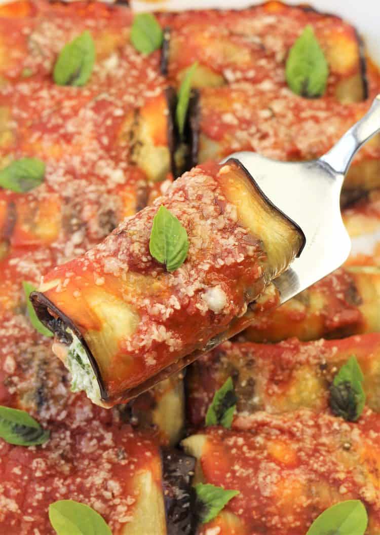 spatula holding an eggplant involtini over baking dish full