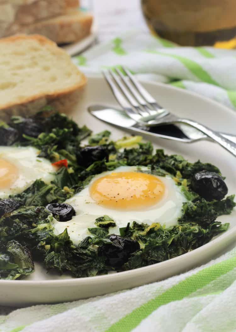 fried eggs with greens on plate with slice of bread and fork and knife