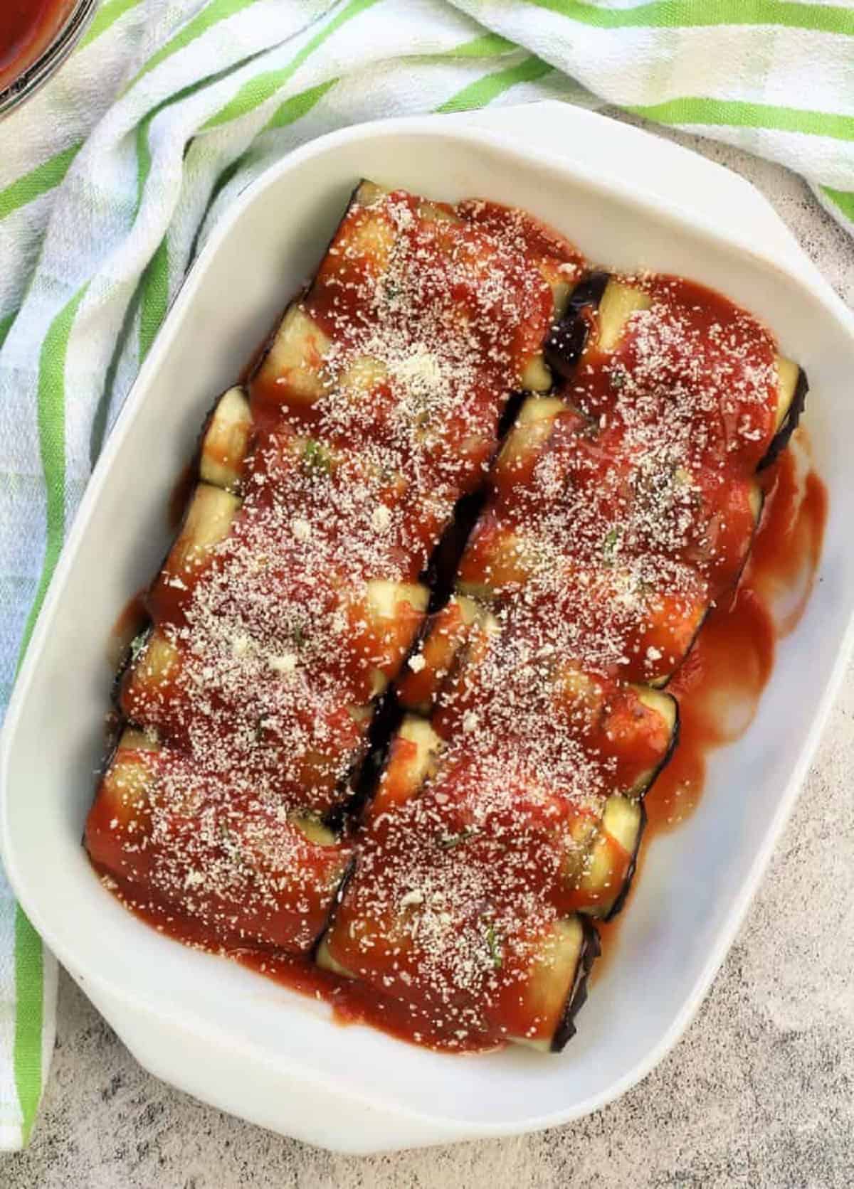 Casserole dish filled with rows of tomato sauce and grated cheese topped eggplant involtini.