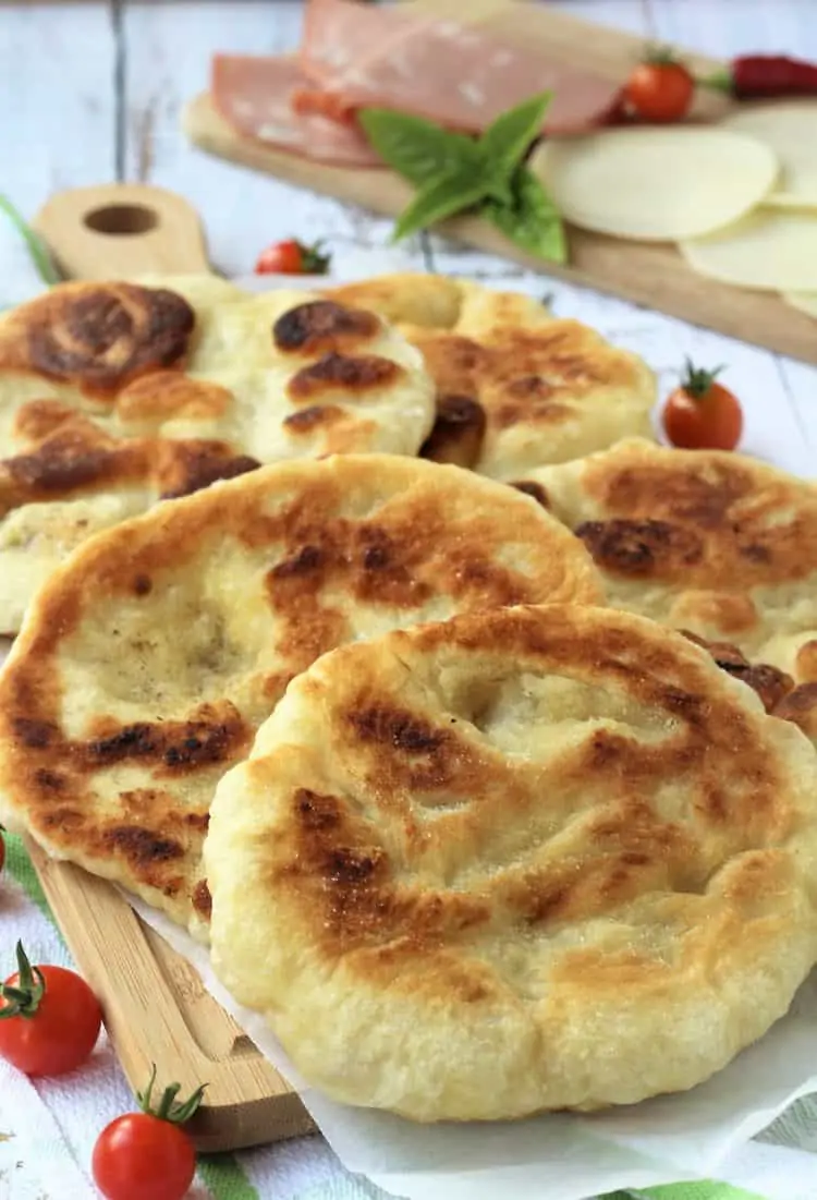 fried pizza dough rounds on wood board served with cherry tomatoes, cheese and mortadella