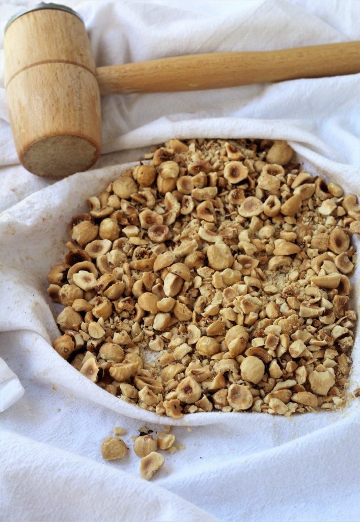 coarsely crushed hazelnuts on dish cloth with meat mallet on side