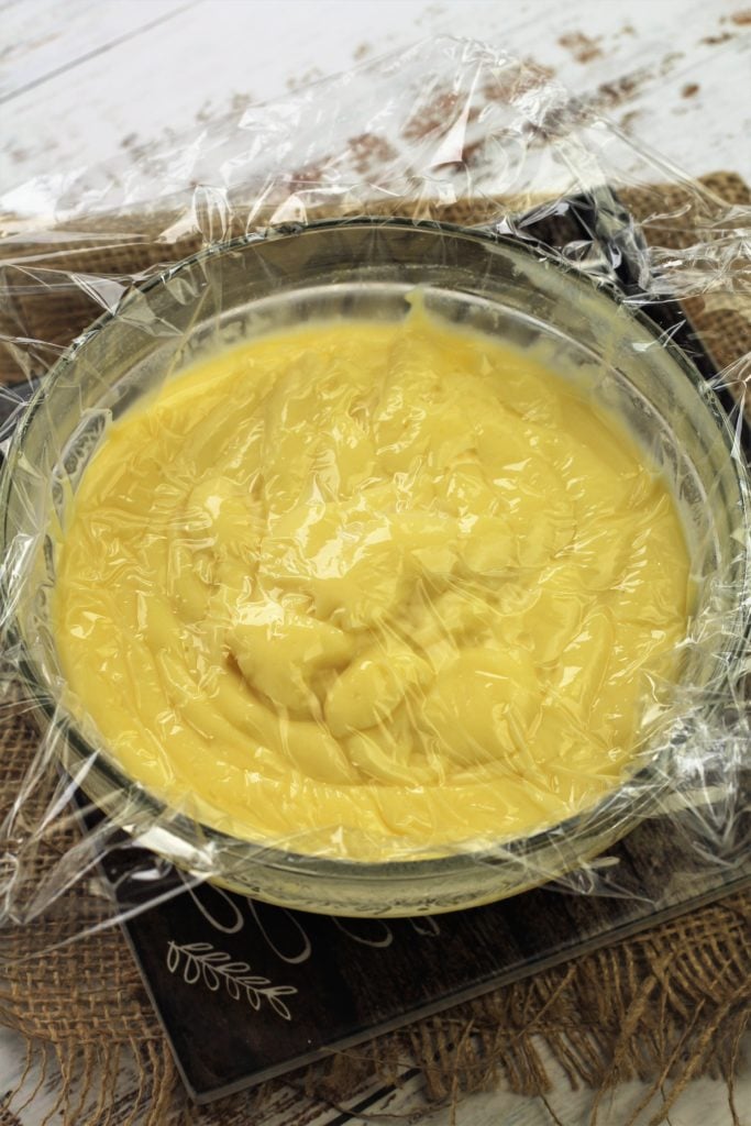 Pastry cream covered with plastic wrap in bowl.
