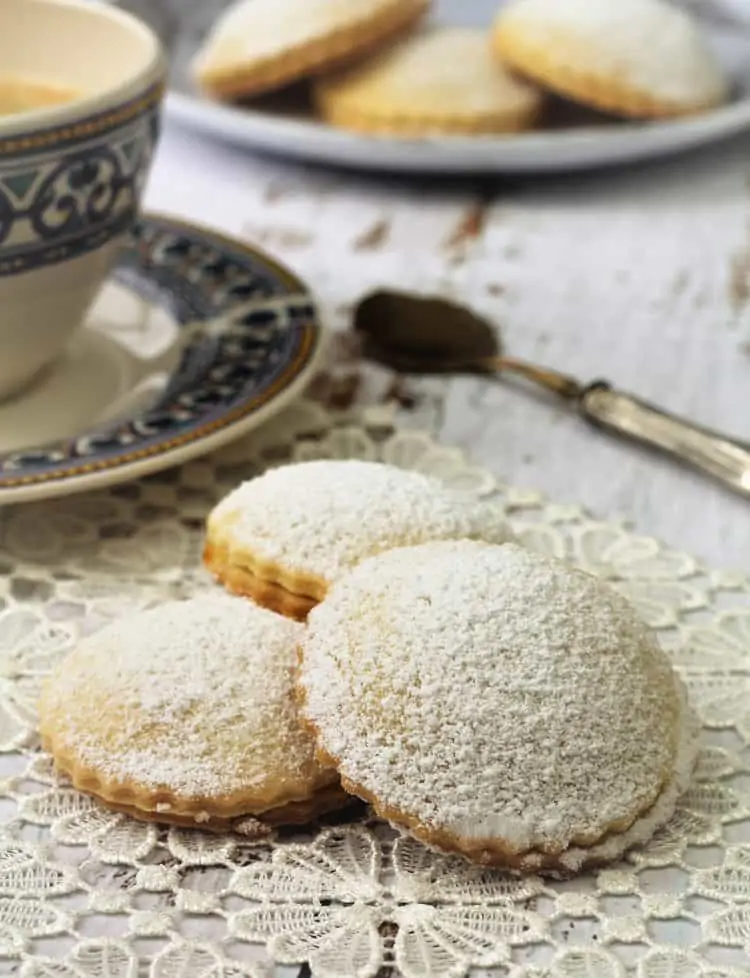 3 genovesi ericine cookies on lace doily next to coffee cup and spoon
