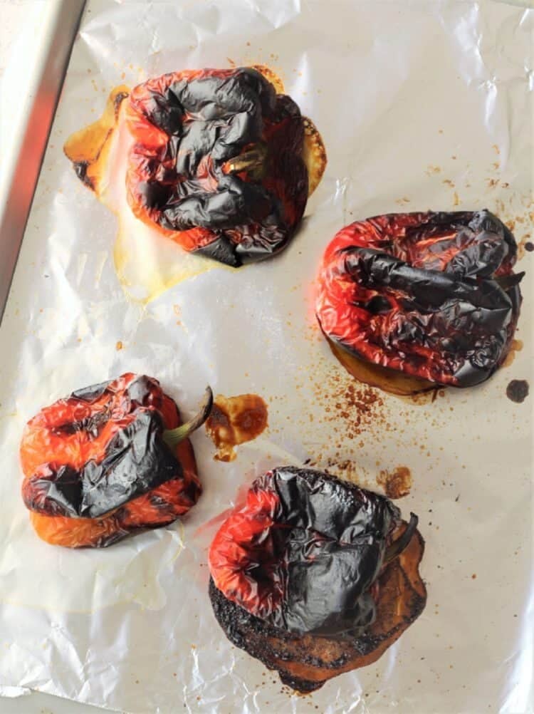 Roasted red peppers with charred skin on foil lined tray.