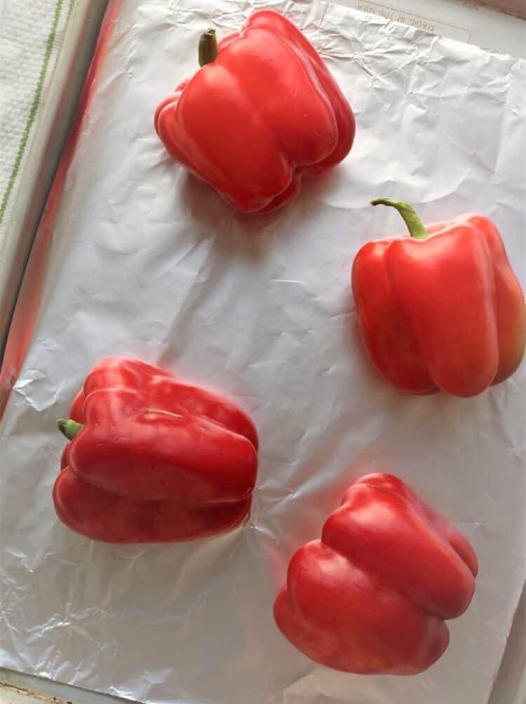 Red bell peppers on foil lined tray for roasting.