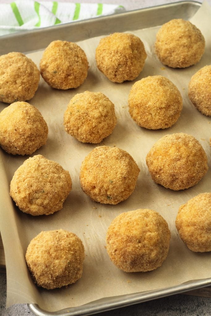 breaded arancini balls on baking sheet ready for frying