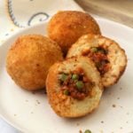 halved arancini filled with meat sauce and peas on white plate