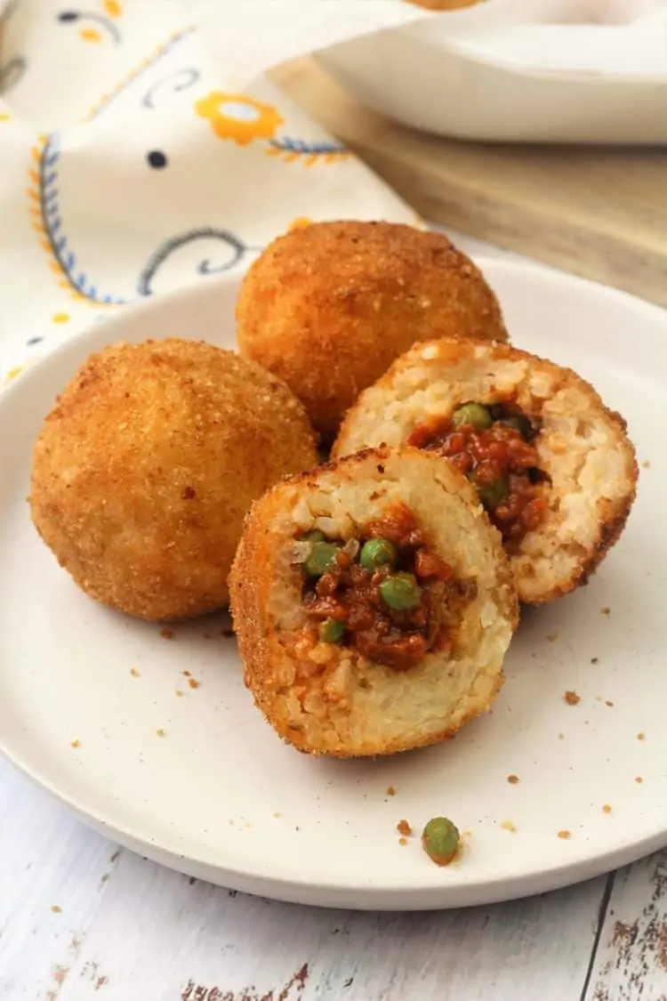 halved Sicilian arancini with meat sauce and peas filling on white plate with 2 whole arancini