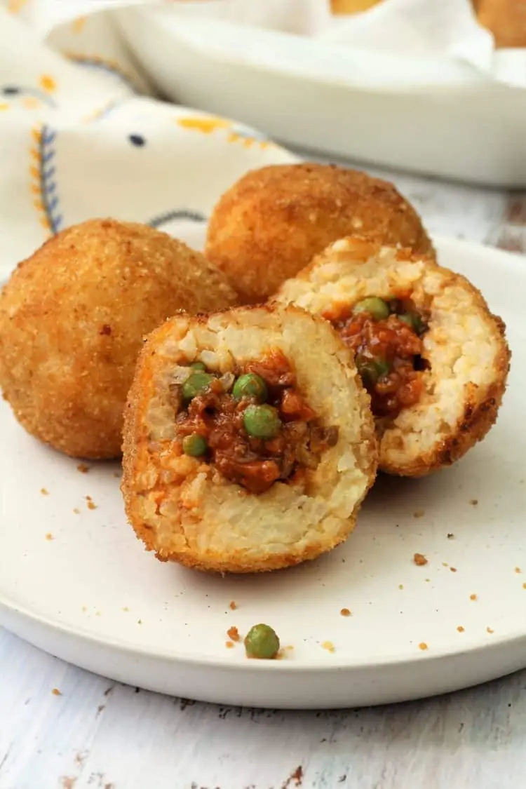 halved arancini with meat sauce and peas filling on plate with 2 whole arancini