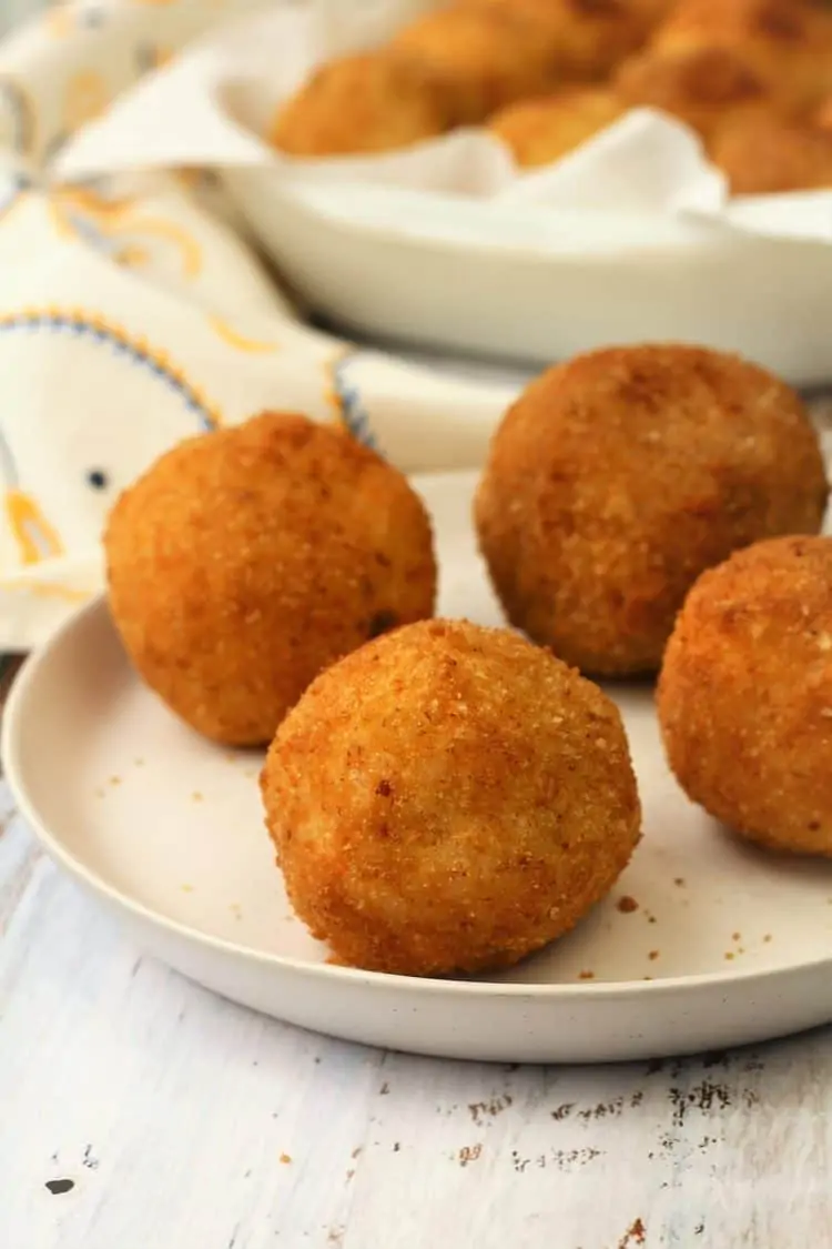4 arancini on white plate with platter full in background